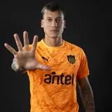 Camiseta de fútbol Puma del Club Atlético Peñarol, modelo GK Away Jersey. Diseño en color naranja con estampado abstracto tonal, cuello redondo y mangas cortas. Incluye logos de Puma, escudo de Peñarol y sponsor Antel en color negro.