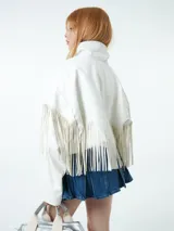 Chaqueta blanca de cuero sintético con cuello camisero, cierre frontal con botones a presión y detalle de flecos en el pecho y las mangas.