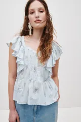 Top de algodón color celeste con estampado floreado, escote corazón y mangas con volados. Presenta detalles de jaretas frontales y corte peplum con vuelo en la parte inferior.