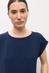 Blusa blanca con textura plumeti, de manga corta y cuello redondo.