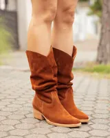 Bota estilo texana de caña alta, confeccionada en cuero gamuzado color marrón óxido. Presenta un diseño de corte en V en la parte superior de la caña, costuras decorativas y un taco bajo de madera.