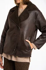 Chaqueta tipo gamulán de calce oversize en color marrón oscuro, con exterior de poliéster y forro de corderito sintético. Presenta cuello de solapa ancha y cierre frontal con botones.