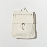 Mochila color blanco con bolsillo frontal con textura símil cuero de cocodrilo y cierre con hebilla metálica. Cuenta con cierre superior con cremallera y asa de mano.
