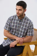 Camisa sport de manga corta con estampa a cuadros en tonos azules, blancos, grises y amarillos, cuello con botones y cierre frontal abotonado.