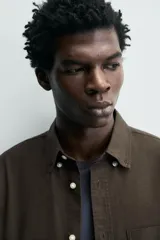 Camisa de corte regular fit confeccionada en tejido de algodón con diseño de rayas verticales. Presenta cuello abotonado, manga larga con puños abotonados, bolsillo plastrón en el pecho y cierre frontal con botones.