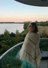 Ruana tejida artesanalmente en lana merino, con diseño de calados geométricos y terminación de flecos largos en el ruedo.