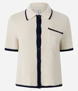 Blusa color crema con cuello inglés y detalles en azul marino, de punto más sostenible, en modelo comfort. Posee cuello inglés, manga corta, abotonado delantero, bolsillo y detalles contrastantes.