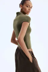 Top de punto suave verde militar, de corte ceñido, cuello alto y mangas cortas con aberturas laterales en las sisas.