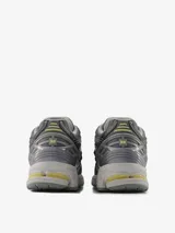 Championes New Balance modelo 1906R, de diseño técnico inspirado en el running, en tonos grises con detalles en amarillo. Presenta una estructura de malla y superposiciones sintéticas, con entresuela amortiguada y suela con tecnología de soporte.