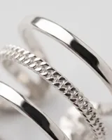 Set de tres anillos de acero plateado con diseños variados: dos lisos con banda delgada y uno central con textura trenzada o de cadena.