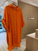 Vestido camisero corto de lino fucsia, fabricado en Italia, con botones en las mangas para recogerlas y botones de nácar. Diseño amplio y cómodo, con un corte irregular que es más largo en la parte trasera que en la delantera.