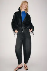 Cazadora de piel 100% color negro de Zara Woman Collection, con cuello subido, manga larga y bolsillos de plastrón con solapa en el delantero. Cuenta con bajo elástico y cierre frontal con cremallera y botones a presión ocultos.