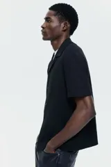 Camisa de manga corta negra H&M en punto jacquard de mezcla de algodón, con cuello abierto y cierre frontal de botones.