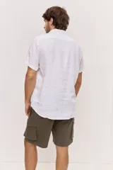 Camisa de manga corta en color blanco, con cuello clásico y cierre frontal de botones al tono. Presenta un diseño versátil de corte regular y textura liviana, ideal para looks frescos.