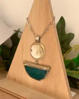 Collar con cadena de acero plateada y un dije colgante de dos partes. La parte superior es un círculo de guampa (cuerno) y la parte inferior es una pieza de ágata verde esmeralda con borde natural, sujeta por una barra metálica.