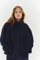 Campera oversized de sherpa suave color azul marino, con cuello elevado, cierre frontal y bolsillos discretos en las costuras laterales. Presenta hombros caídos y mangas largas amplias.