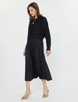 Conjunto compuesto por un buzo de tejido calado con cuello redondo y mangas largas, y un vestido midi de satén con falda plisada. Ambas piezas son de color negro y pueden combinarse o utilizarse por separado.