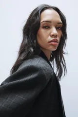 Blazer corto de corte oversize con estampado de cuadros, cuello con solapa de muesca, manga larga y cierre frontal cruzado con un botón. Cuenta con bolsillos decorativos de vivo en el frente y forro interior.