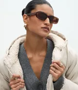 Campera parka de Marfinno confeccionada en PU con textura gomosa, color beige. Cuenta con capucha, forro interior de peluche sintético, cierre frontal con solapa y botones a presión, y bolsillos delanteros grandes con solapa.