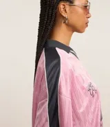 Remera rosa con cuello polo gris y rayas verticales. Estampado frontal con la palabra "gobline" en letras cursivas y la frase "in my best era". Diseño oversized con mangas cortas y recortes laterales en color negro.