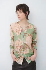 Camisa de manga larga con fondo verde y estampado floral en tonos rosados y beige, cuello redondo con pequeña abertura en V y cierre frontal con botones.