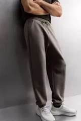 Pantalón jogger de entrenamiento, corte regular fit, color verde oliva oscuro. Confeccionado en tejido técnico compacto de algodón con elasticidad y efecto neopreno. Presenta cintura elástica ajustable con cordón blanco, bolsillos frontales y un bolsillo lateral con cierre de cremallera. El bajo termina en puño.