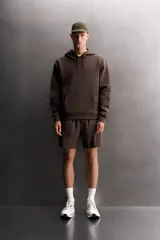 Sudadera de hombre Zara Athleticz de ajuste relajado (relaxed fit), color marrón, confeccionada en tejido técnico compacto con mezcla de algodón y elasticidad. Cuenta con cuello con capucha ajustable con cordones negros, manga larga, bolsillo frontal tipo canguro con un pequeño bolsillo termofijado con cierre, y acabados con rib en puños y cintura.