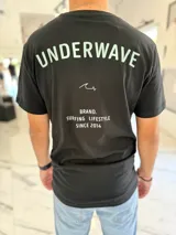 Remera negra de corte clásico con estampado gráfico en la espalda con el texto "Underwave Brand. Surfing Lifestyle Since 2014" en colores verde claro y blanco.