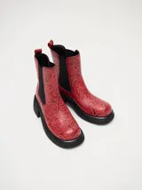 Bota tipo chelsea de cuero vacuno en color rojo con estampado floral grabado en negro. Presenta paneles laterales elásticos, suela de plataforma y taco cuadrado en color negro.