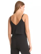 Enterito negro de crepe con escote en V, breteles finos ajustables y una capa suelta en la parte superior. La cintura es definida con corte anatómico y el pantalón tiene pierna ancha de caída fluida. Cierre invisible en la espalda.