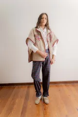 Poncho de paño color beige con flores bordadas en el frente y detalles de costura artesanal en los bordes en color bordó. Cuenta con bolsillos laterales y cierre frontal con botones de madera.