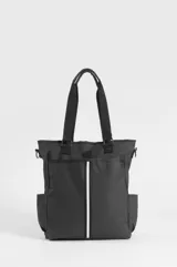 Bolso tipo tote negro confeccionado en PVC y poliéster, con compartimento principal con cierre, bolsillos laterales y bolsillo trasero con cierre. Incluye asas superiores de mano, correa ajustable removible y un estuche removible para paleta de pádel con detalle de franja vertical blanca.