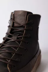 Championes de caña alta confeccionados en cuero marrón oscuro, con cordones al tono y suela de goma color caramelo.