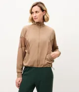 Campera deportiva rompevientos Get Over de color beige, con cuello alto, cierre frontal y recortes de tul transparente en las mangas y hombros. Cuenta con cintura ajustable.