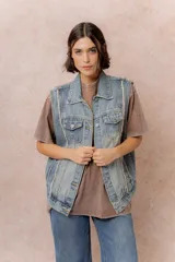 Chaleco de jean con diseño oversized y lavado vintage. Presenta cuello camisero, cierre frontal con botones metálicos, bolsillos superiores con tapa y botón, bolsillos laterales y terminaciones desflecadas en las sisas.