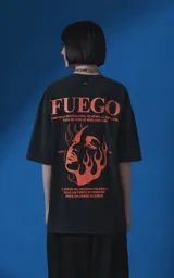 Remera de manga corta con cuello redondo y calce oversize, color negro con efecto nevado. Presenta una estampa frontal en color naranja con diseño gráfico de un rostro rodeado de llamas y texto tipográfico.