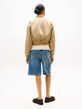 Campera bomber corta de color beige, con cierre frontal, cuello estilo béisbol, puños y bajo de punto canalé. Presenta un logo bordado en el pecho.