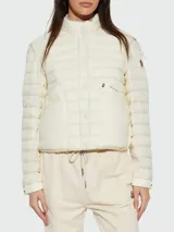Campera acolchada Moncler modelo Madulains, color blanco hueso, con cuello alto, cierre frontal con botones a presión y diseño ligero. Presenta detalles de costuras horizontales y logo de la marca en la manga.