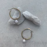 Aros de acero quirúrgico dorados en formato de argolla, con un dije colgante de perla natural.