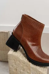 Botinetas de cuero vacuno con textura tipo reptil en color marrón chocolate. Presentan un diseño de caña media con cierre posterior, puntera redondeada y suela de goma con taco cuadrado robusto.