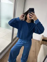 Conjunto deportivo de dos piezas color azul, compuesto por un buzo de cuello redondo y mangas largas, y un pantalón de corte ancho con cintura elástica. El buzo presenta un diseño reversible con costuras visibles.