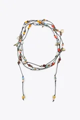 Collar largo de cordón negro con nudos, adornado con abalorios de diversos colores y formas, junto con charms metálicos dorados con forma de corazones y puntas. Su diseño versátil permite utilizarlo en múltiples posiciones.