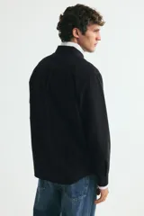 Camisa de algodón estilo Oxford, color negro, con cuello americano abotonado, bolsillo en el pecho y cierre frontal con botones blancos.