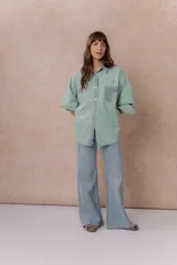 Camisa de denim color verde menta con calce relajado, cuello clásico, cierre frontal con broches metálicos, mangas largas y bolsillo aplicado en el pecho, con detalles en tono gris azulado a contraste en cuello, cartera, bolsillo y puños.