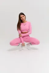 Conjunto deportivo de dos piezas compuesto por un top de manga larga con cuello redondo y detalle de tejido calado en el pecho, y calzas de tiro alto. Ambas prendas presentan un diseño sin costuras en un tono rosado vibrante.
