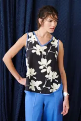 Top sin mangas de color blanco con escote en V y diseño holgado. Presenta un estampado artístico frontal en tonos azul y rojo, con terminaciones de vivo a contratono en color marrón.