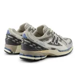 Championes New Balance modelo 1906R, unisex, con capellada de malla color crema, superposiciones de cuero sintético gris y detalles en azul. Cuenta con amortiguación N-ergy, entresuela ACTEVA LITE y talón ABZORB SBS.