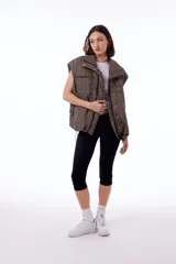 Chaleco puffer con estampado de celebridades, impermeable y forrado en tafeta negra. Tiene dos bolsillos frontales, bolsillos laterales ocultos, cierre desmontable, broches snap y elástico ajustable con tanca en el ruedo.