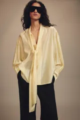 Camisa de corte holgado confeccionada en tejido satinado con mezcla de lyocell. Presenta cuello redondo con escote en pico y lazada frontal integrada. Cuenta con mangas largas abullonadas terminadas en puños anchos y bajo recto.