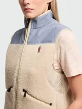 Chaleco de diseño híbrido con cuerpo de tejido de peluche en color beige y canesú superior de cambray en tono azul claro. Presenta cierre frontal completo, bolsillos laterales con cierre y logo de la marca bordado en el pecho.